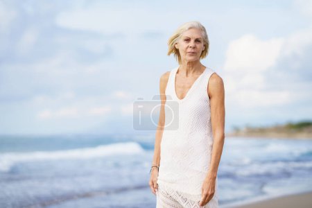 Foto de Retrato de una mujer madura sonriente caminando por la playa. Mujer mayor disfrutando de su retiro en un lugar junto al mar. - Imagen libre de derechos