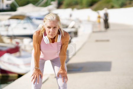 Photo for Mature sportswoman taking a break during exercise. Concept of healthy living in the elderly. Senior woman in fitness clothing. Older female doing sport to keep fit. - Royalty Free Image