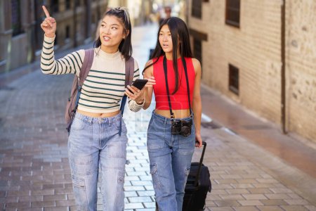 Foto de Dos jóvenes chinas que pasan guiadas por el GPS de su smartphone, por las calles de Granada, España. Concepto de personas asiáticas que viajan por Europa. - Imagen libre de derechos