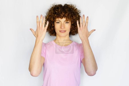 Téléchargez les photos : Femme aux cheveux bouclés positive montrant le numéro dix sur les doigts tout en levant les bras et en regardant la caméra sur fond blanc - en image libre de droit