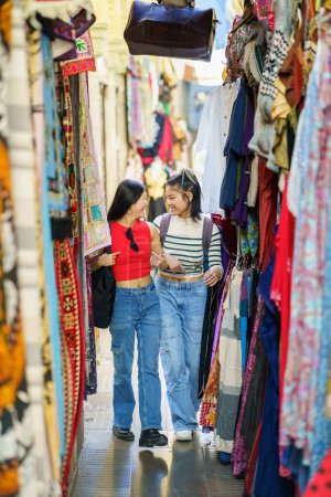 Téléchargez les photos : Souriantes jeunes femmes amis en vêtements décontractés marchant le long du magasin de vêtements colorés sur le marché de rue en ville pendant les vacances d'été - en image libre de droit