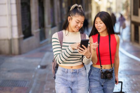 Photo for Two young Chinese females passing by guided by the GPS of their smartphone, through the streets of Granada, Spain. Concept of Asian people traveling in Europe. - Royalty Free Image