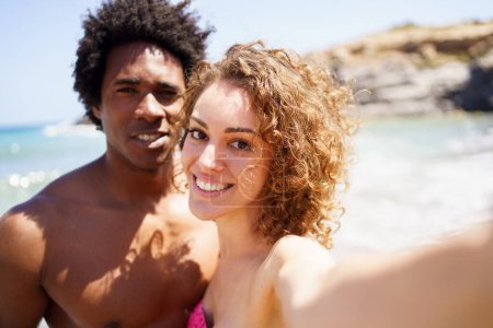 Photo for Delighted young woman outstretching hand towards camera while taking selfie with black boyfriend against sea and rocky cliff - Royalty Free Image