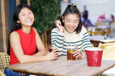 Photo for Two young Chinese girls having a drink on the terrace of a typical bar in Granada. Concept of Asian people traveling in Europe. - Royalty Free Image
