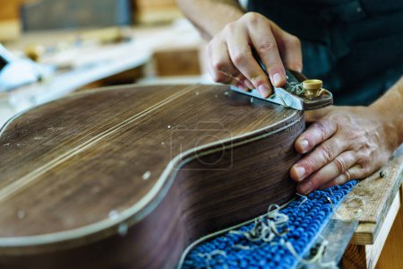 Photo for Crop craftsman using plane to shave traditional Spanish flamenco guitar on workbench in workshop - Royalty Free Image