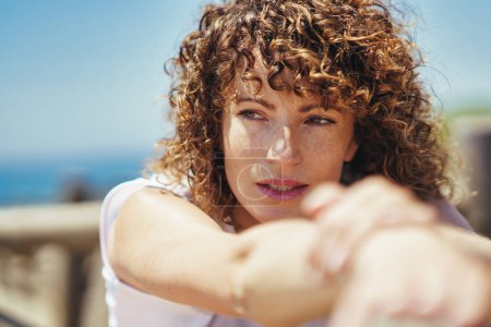 Photo for Side view of young female with curly hair looking away thoughtfully while leaning on fence against blurred background in daytime - Royalty Free Image