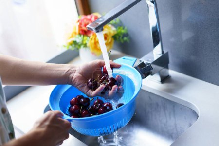 Photo for From above of crop unrecognizable female washing ripe cherries in plastic colander under water from faucet in kitchen sink - Royalty Free Image