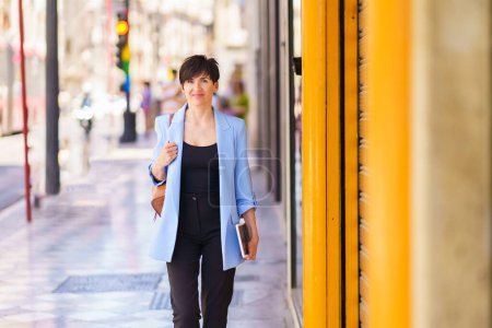 Foto de Mujer alegre de confianza en traje formal de moda mirando a la cámara mientras está de pie en el pasillo de la calle de la ciudad contra el fondo borroso - Imagen libre de derechos