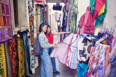 Téléchargez les photos : Deux jeunes Chinoises visitant Grenade, en Espagne, regardant des vêtements typiques dans les magasins d'artisanat typiques de l'Alcaicer a, vieux souk musulman de Grenade. Concept de personnes asiatiques voyageant en Europe. - en image libre de droit