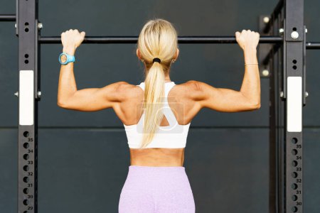 Photo for Back view of anonymous female athlete doing pulls up on horizontal bar during workout in gym - Royalty Free Image