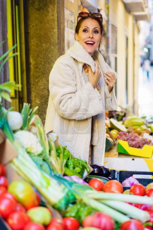 Foto de Vista lateral de la mujer joven en ropa de abrigo, y anteojos en la cabeza mirando a la cámara mientras está de pie en el establo con una variedad de verduras y frutas en el día soleado - Imagen libre de derechos