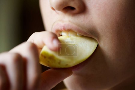 Photo for Closeup of crop unrecognizable young girl biting fresh juicy apple piece at home - Royalty Free Image