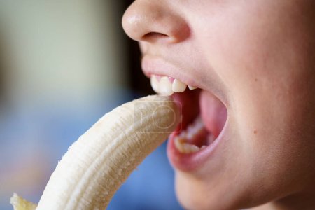 Photo for Crop unrecognizable teenage girl with mouth open about to eat fresh peeled banana at home - Royalty Free Image