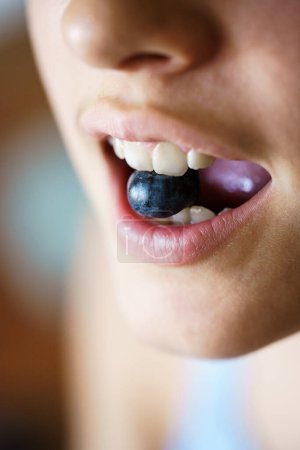 Photo for High angle closeup of unrecognizable crop young girl holding fresh blueberry between teeth at home - Royalty Free Image
