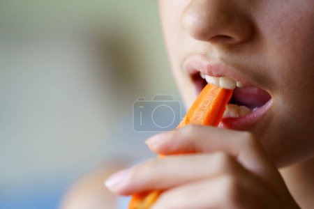 Téléchargez les photos : Gros plan de récolte anonyme adolescent fille mordre tranche de carotte fraîche à la maison - en image libre de droit