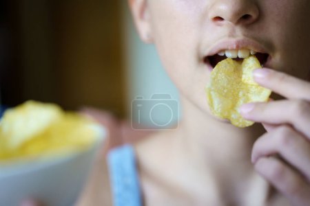 Photo for Closeup of unrecognizable young girl eating crispy potato chip at home - Royalty Free Image