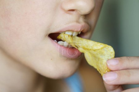 Photo for Closeup of crop anonymous young girl biting crunchy potato chip at home - Royalty Free Image