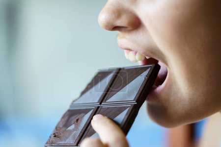 Photo for Crop anonymous teenage girl with mouth open eating chocolate bar at home - Royalty Free Image