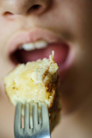 Photo for Closeup of crop anonymous young girl about to eat delicious potato omelette from fork at home - Royalty Free Image