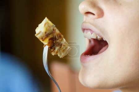 Photo for Crop unrecognizable teenage girl with mouth open about to eat yummy potato omelette from fork at home - Royalty Free Image