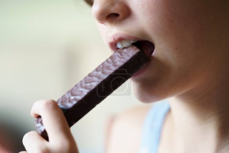 Photo for Closeup of crop unrecognizable teenage girl eating healthy protein bar at home - Royalty Free Image