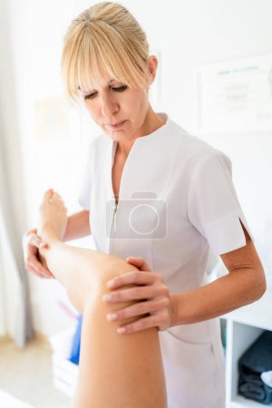 Téléchargez les photos : Physiothérapeute professionnel effectuant un massage de réadaptation sur la jambe d'une patiente lors d'un rendez-vous dans un centre clinique moderne - en image libre de droit