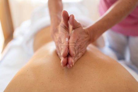 Foto de Enfoque suave de cultivo anónimo terapeuta de masaje femenino frotando la espalda de la mujer con las manos apretadas durante la rehabilitación - Imagen libre de derechos