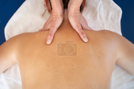 Foto de Vista superior de la cosecha anónima masajista femenina frotando el cuello y los hombros del cliente acostado en la toalla durante la sesión de rehabilitación - Imagen libre de derechos