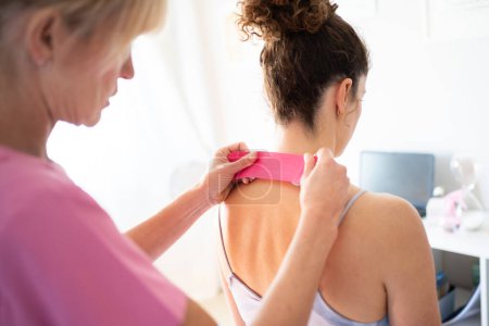 Photo for Crop focused professional osteopath applying kinesiology tape on back of neck of unrecognizable young female patient during physiotherapy session in clinic - Royalty Free Image