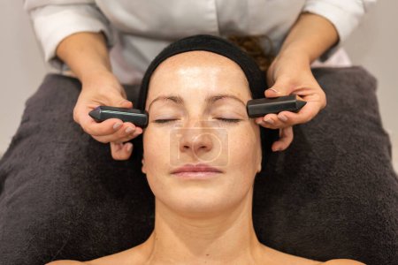 Photo for Top view of crop anonymous female cosmetician massaging face of adult woman with black crystals during skincare procedure in beauty salon - Royalty Free Image