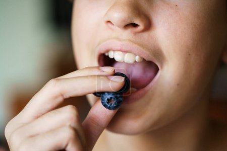 Photo for Closeup of unrecognizable teenage girl with mouth open eating yummy blueberries at home - Royalty Free Image