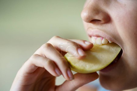 Photo for Closeup of anonymous teenage girl eating fresh apple slice at home - Royalty Free Image
