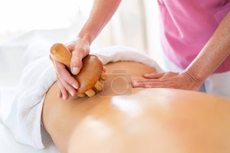 Téléchargez les photos : Cultivez le massage anonyme du thérapeute avec un outil de thérapie en bois sur le dos d'un client anonyme lors d'une séance de physiothérapie en clinique d'ostéopathie - en image libre de droit
