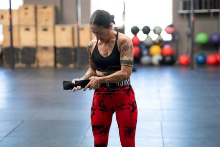 Photo for Mature modern woman with tattoos putting on a belt to prevent injuries while lifting deadlifts - Royalty Free Image