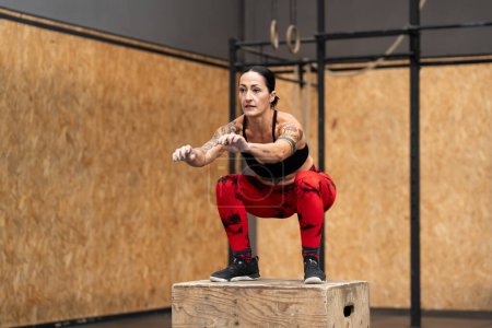 Photo for Horizontal photo with copy space of a tattooed woman exercising using box in a cross training gym - Royalty Free Image