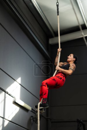 Foto de Foto vertical de una mujer fuerte trepando la cuerda en un gimnasio de entrenamiento cruzado - Imagen libre de derechos