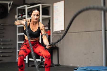 Foto de Mujer madura fuerte haciendo ejercicio con cuerdas de batalla en un gimnasio de entrenamiento cruzado - Imagen libre de derechos