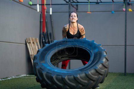 Foto de Foto frontal de una mujer madura fuerte levantando una rueda en un gimnasio - Imagen libre de derechos