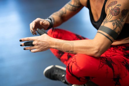 Foto de Primer plano de atleta protegiendo sus dedos con cinta adhesiva mientras está sentada en el gimnasio - Imagen libre de derechos