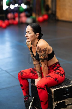 Photo for Vertical photo of a tired athlete resting sitting on a box in a cross training gym - Royalty Free Image