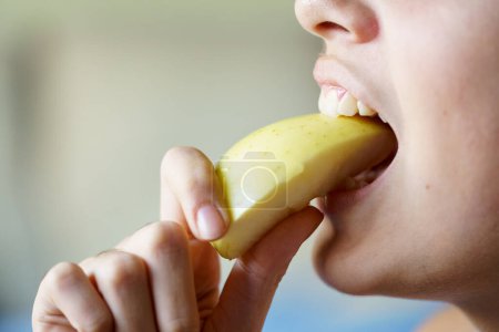Photo for Closeup of crop unrecognizable teenage girl eating apple slice at home - Royalty Free Image