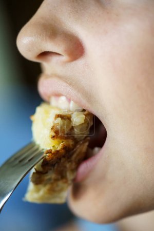 Photo for Closeup of crop unrecognizable teenage girl eating fresh delicious Spanish potato omelette from fork at home - Royalty Free Image