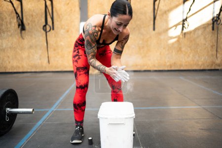 Photo for Mature fit woman with tattooed arms applying magnesium powder to her hands for weightlifting - Royalty Free Image