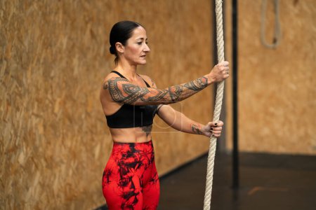 Téléchargez les photos : Femme forte mature sur le point de commencer à grimper une corde dans une salle de gym - en image libre de droit