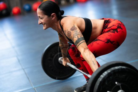 Foto de Sonriente mujer deportiva madura levantamiento de pesas en un gimnasio de entrenamiento cruzado - Imagen libre de derechos