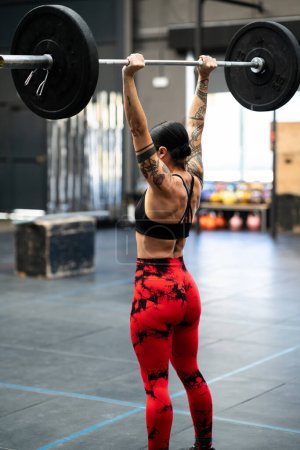 Photo for Vertical rear view of a mature sportive and strong woman bodybuilding in a gym - Royalty Free Image