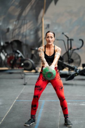 Photo for Vertical photo of a mature sportive woman performing kettlebell swing exercise in a gym - Royalty Free Image