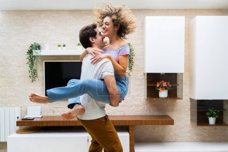 Photo for Side view of cheerful young couple in casual clothes smiling and hugging while having fun at home - Royalty Free Image