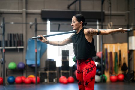 Horizontales Foto mit Kopierraum einer erwachsenen starken Frau, die sich in einem Fitnessstudio mit der Stange nach hinten streckt