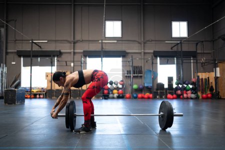 Foto de Fotografía horizontal con espacio de copia de una mujer en forma preparando un bar y ascensores para levantamiento de pesas en un gimnasio de entrenamiento cruzado - Imagen libre de derechos